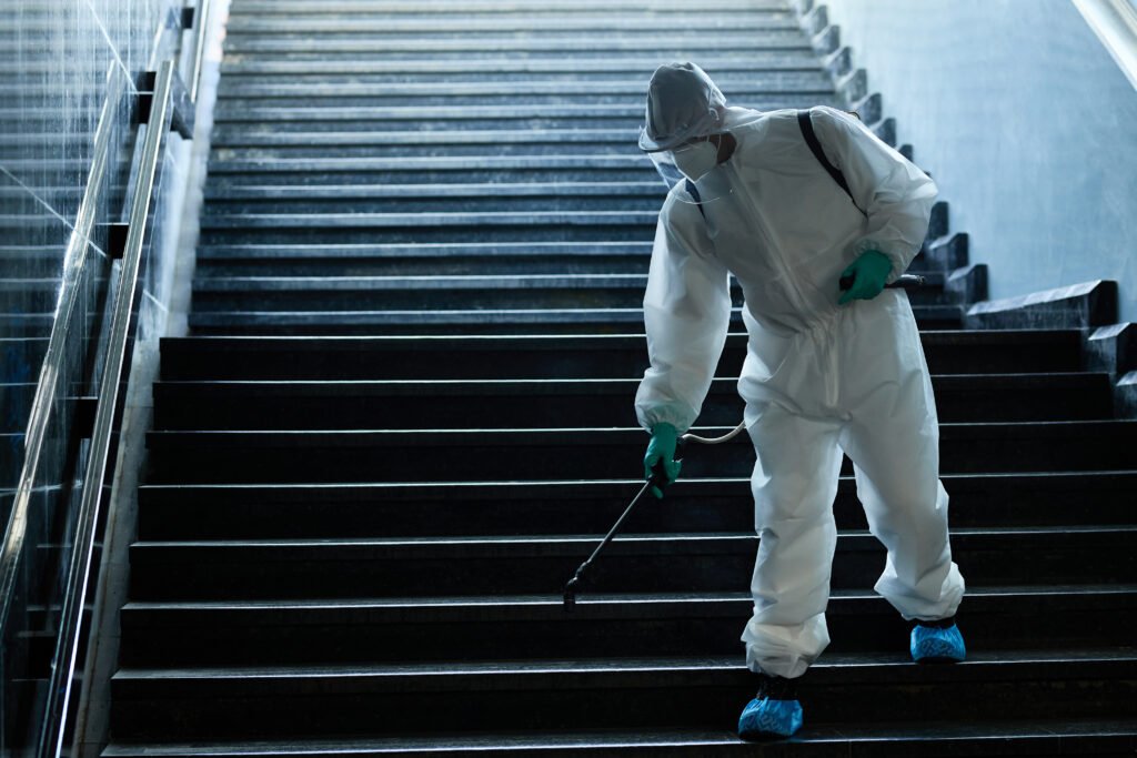 Man in protective suit disinfecting staircase of underground passage in order to prevent the spread of coronavirus.